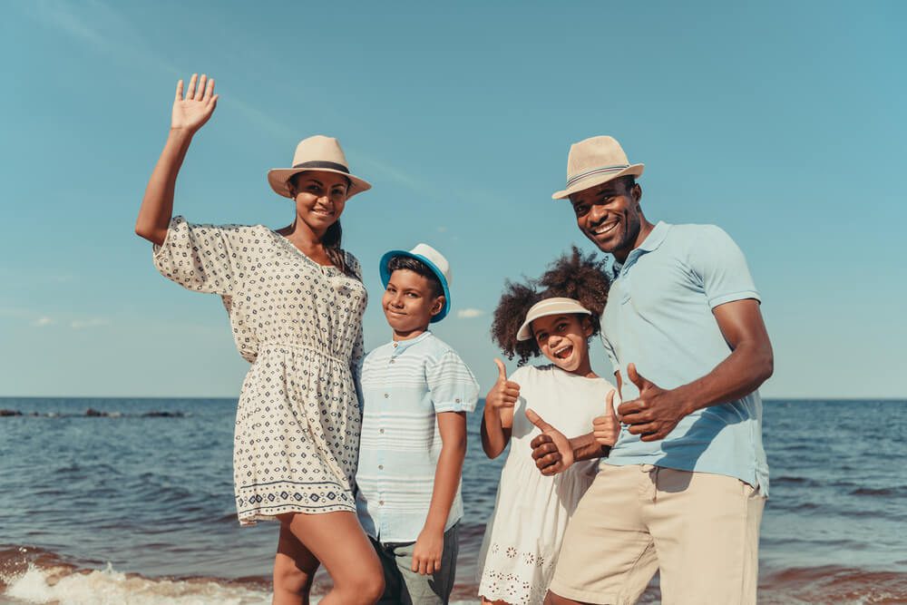 A family of four smiles while on the beach, which is one of the best 10 family vacation ideas during their trip along the Florida Gulf Coast.