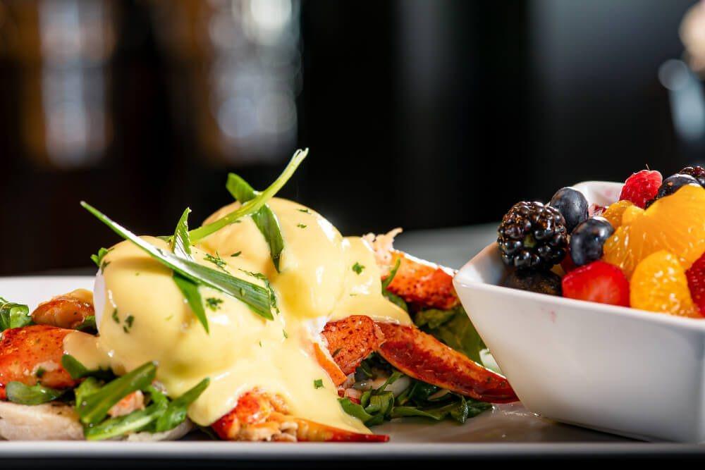 A plate of crab eggs benedict, next to a bowl of fruit, is pictured and is one of the dishes you can make in your FL beach house.